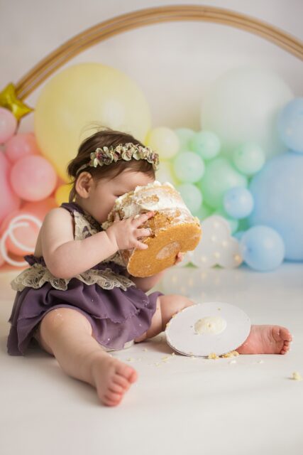 Jackson Missouri newborn photographer, Perryville cake smash photographer, Cape Girardeau newborn photographer, baby picking up cake, cake smash photos, rainbow backdrop, studio first birthday