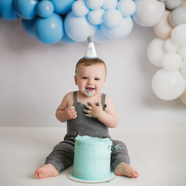 perryville newborn photographer, perryville cake smash photographer, Cape Girardeau cake smash photographer, baby with blue cake, cake face, baby boy smiling, boy photoshoot, first birthday balloon banner