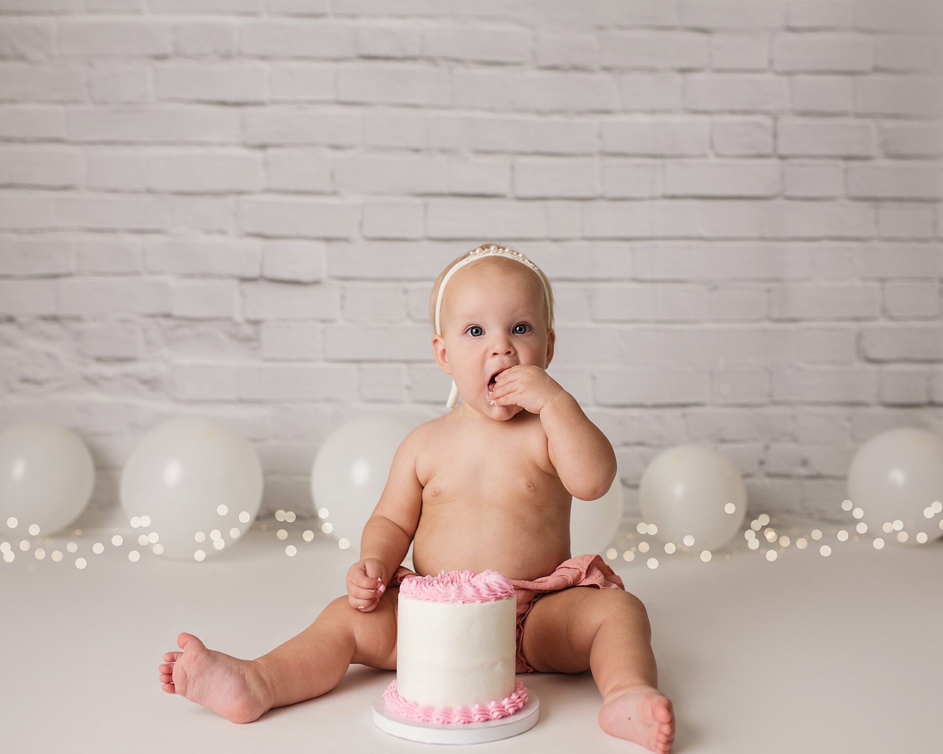 Jackson Missouri photographer, Perryville cake smash photographer, Cape Girardeau newborn photographer, cake smash photoshoot, white brick backdrop, simple cake smash set up, baby eating cake