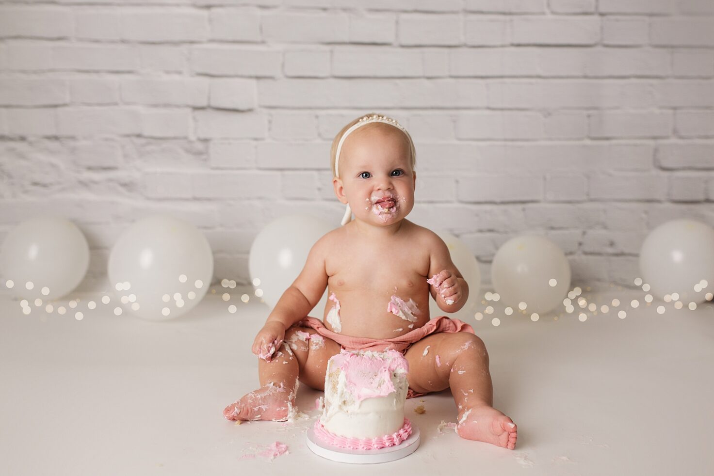 Jackson Missouri newborn photographer, Perryville cake smash photographer, Cape Girardeau newborn photographer, cake smash photoshoot, white brick backdrop, simple cake smash set up, baby eating cake and smiling