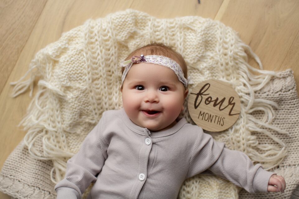 Cape Girardeau newborn photographer, Perryville newborn photographer, milestone photoshoot, wood floor, baby laying wood floor, 4 months old, big smile, purple onsie