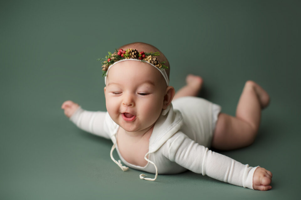 perryville newborn photographer, Cape Girardeau newborn photographer, green backdrop, tummy time, Christmas photoshoot, big smile, pine cone headband