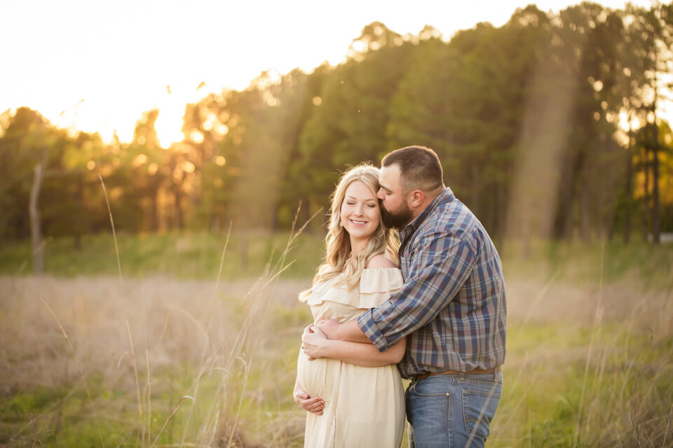 Cape Girardeau maternity photographer, perryville maternity photographer, dad kissing mom, mom holding baby belly, sunset image, sunset photoshoot, grass field