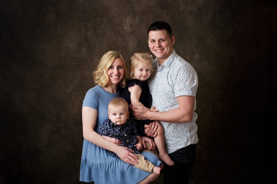 st Louis newborn photographer, farmington Missouri Newborn photographer, cape girardeau Missouri Newborn photographer, perryville family photographer, looking at camera, family of 4, brown studio backdrop, studio family portraits